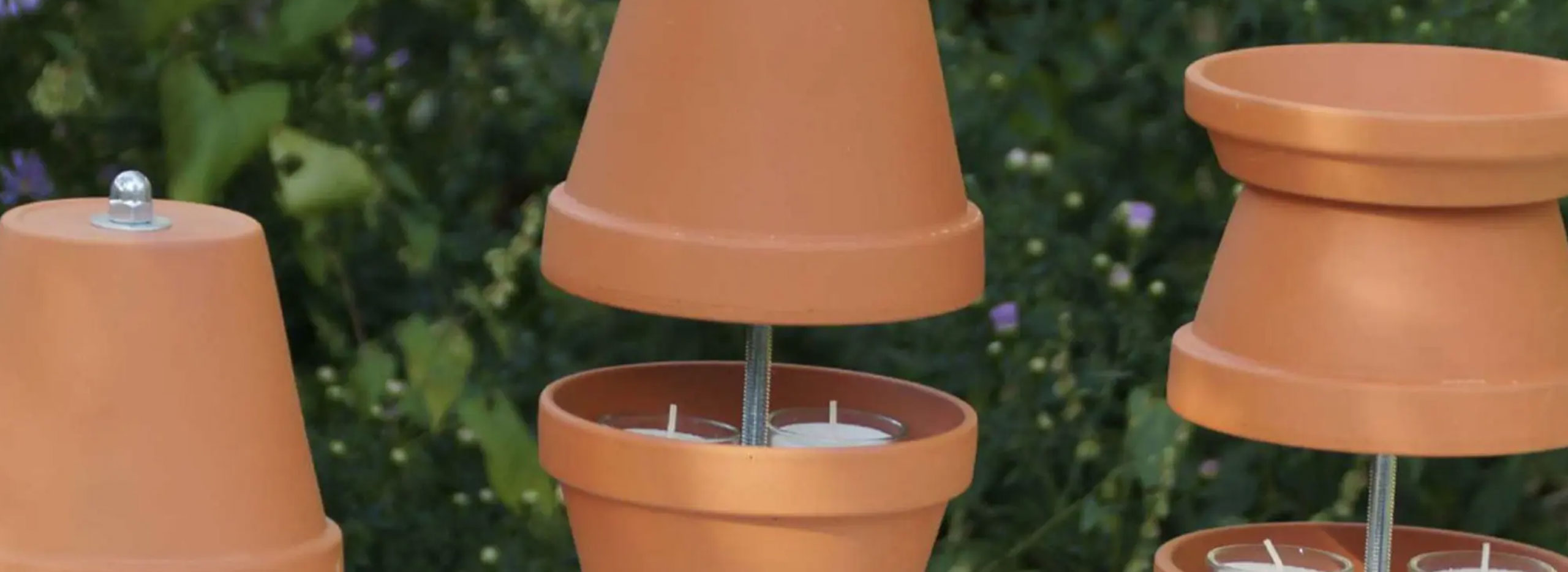 Mehrere übereinandergestapelte Terrakotta-Töpfe sind mit einer Metallstange verbunden; im unteren Topf stehen Teelichter, die als einfache DIY-Teelichtheizung dienen.