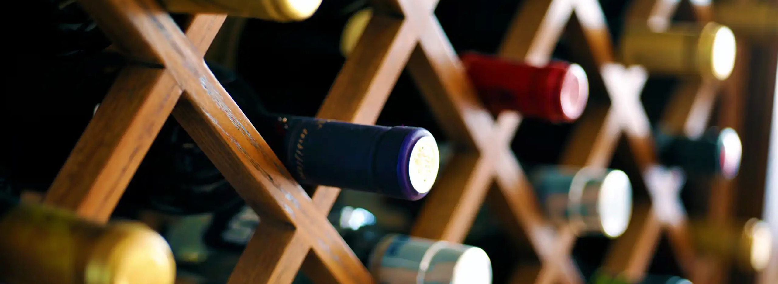 Holzregal mit schräg gelagerten Weinflaschen in verschiedenen Farben. Symbolbild für das Thema Weinregal selber bauen.