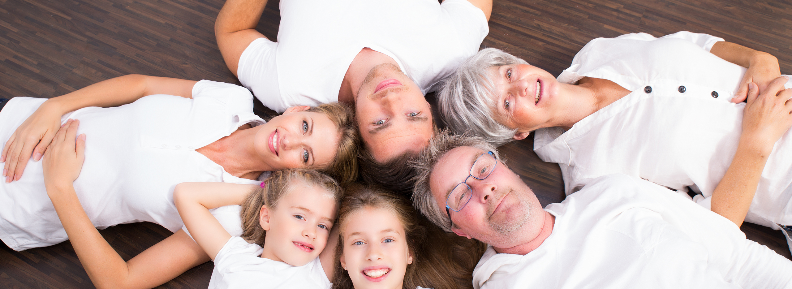 Familien verschiedener Generationen liegen gemeinsam auf dem Boden und lächeln. Symbolbild für das Thema Mehrgenerationenhaus.