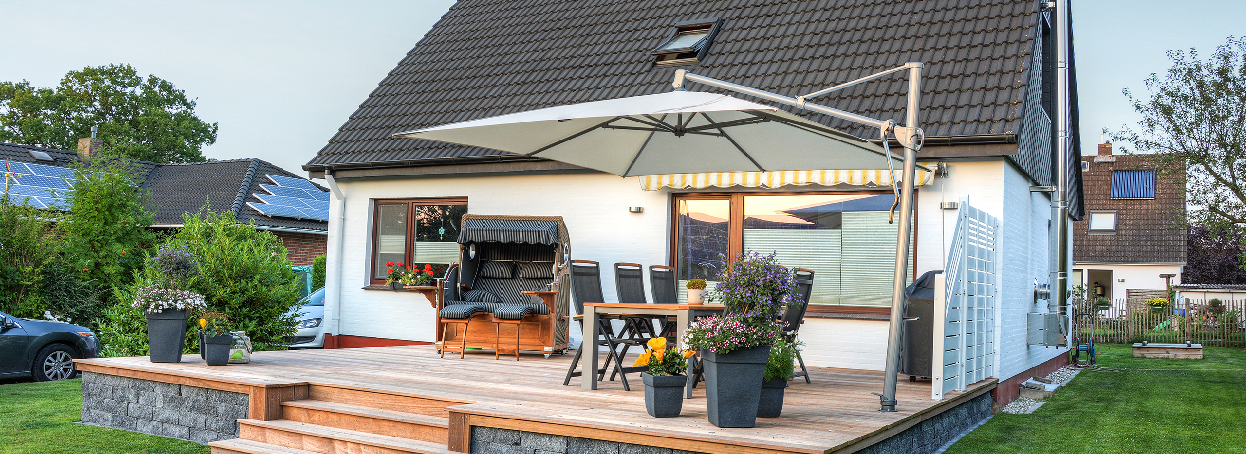 Gemütliche Terrasse mit Holzbelag an einem Einfamilienhaus, ausgestattet mit großem Sonnenschirm.