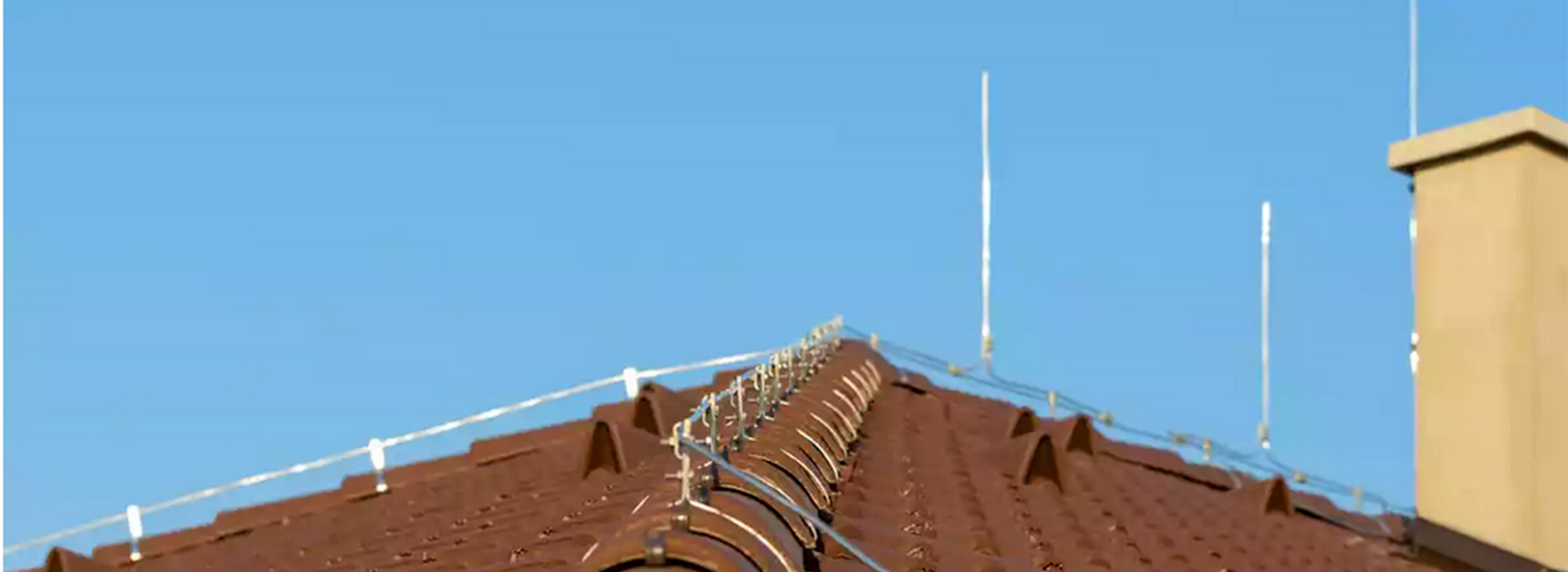 Das Bild zeigt ein Hausdach mit Blitzableiter. Sichtbare Fangleitungen und Metallstäbe schützen Gebäude zuverlässig vor Blitzeinschlägen.