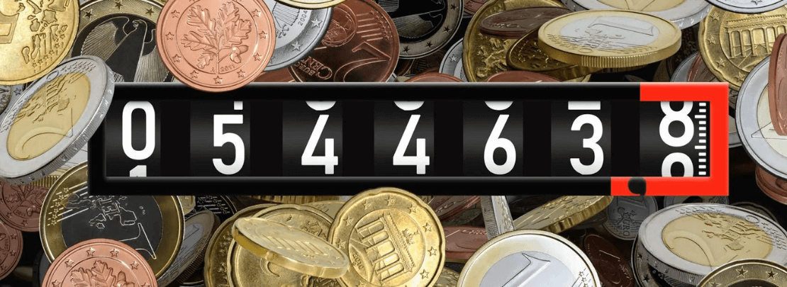 Das Bild zeigt einen analogen Zähler vor einem Hintergrund aus Euromünzen – Symbol für Gasverbrauch und Kosten.