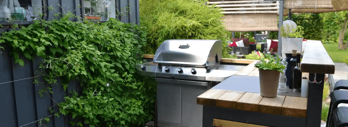 Moderne Outdoor-Küche mit Edelstahl-Gasgrill, Holzarbeitsfläche und Kräutertopf – ideal für gemütliches Grillen im Garten.