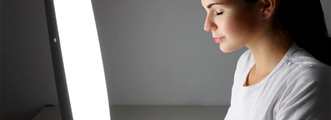 Frau sitzt vor einer Tageslichtlampe und nutzt Lichttherapielampe zur Behandlung von Winterdepression.