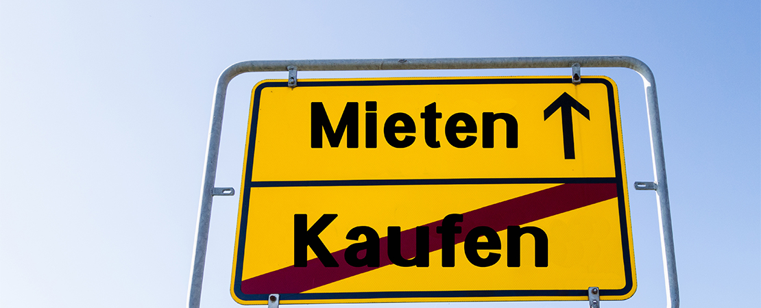 Verkehrsschild mit den Worten „Mieten“ und durchgestrichenem „Kaufen“ vor blauem Himmel, symbolisiert Trend zum Mieten statt Kaufen.