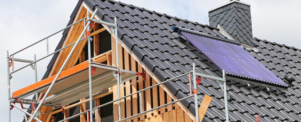 Ein Wohnhaus mit Baugerüst wird energetisch saniert, auf dem Dach ist eine Solaranlage installiert.