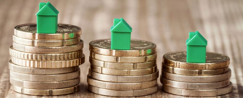Drei Stapel mit Münzen in unterschiedlicher Höhe, auf jedem Stapel steht ein kleines grünes Haus.